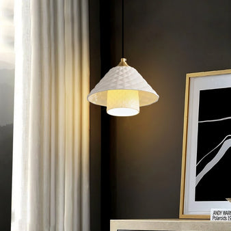 "A modern pendant light with a textured ceramic shade hanging in a room with artwork."