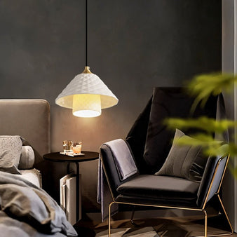 "A modern pendant light with a textured ceramic shade hanging above a bedroom seating area."