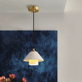 "A modern pendant light with a textured ceramic shade hanging in a room with a blue wall."