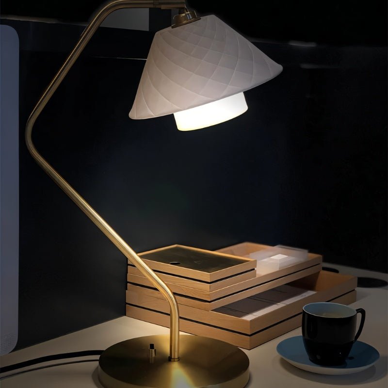 Close-up of Ocris Table Lamp lit on a desk, showcasing brass structure and textured ceramic shade for cozy indoor lighting.