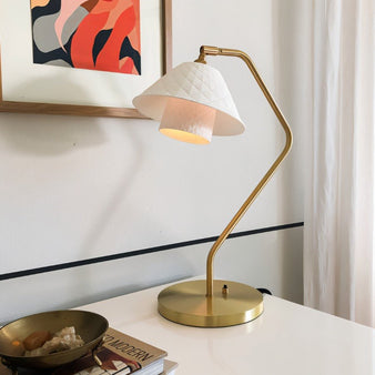 "Modern brass table lamp with white quilted ceramic shade on a desk, illuminating a workspace."