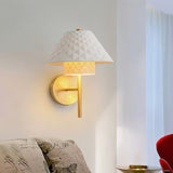 "A modern brass wall lamp with a textured ceramic shade illuminating a bedroom."