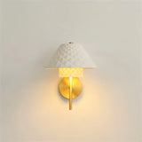 "A modern brass wall lamp with a textured ceramic shade on a white wall."