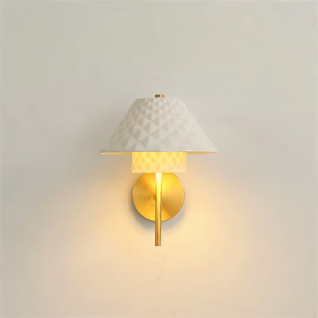"A modern brass wall lamp with a textured ceramic shade on a white wall."