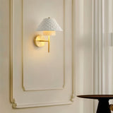 "A modern brass wall lamp with a textured ceramic shade on a panelled wall."