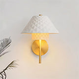 "A modern brass wall lamp with a textured ceramic shade on a light wall."