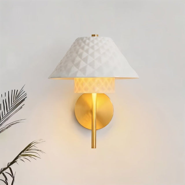 "A modern brass wall lamp with a textured ceramic shade on a light wall."