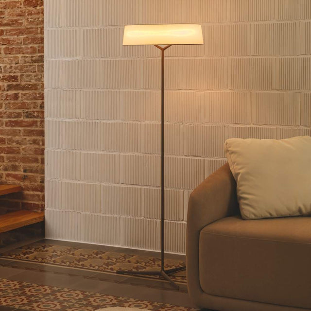 "A modern floor lamp with a rectangular fabric shade and a slim stand illuminates a corner of a bedroom with textured walls."