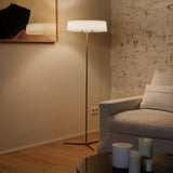 "A transitional floor lamp with a rectangular fabric shade and a slim, dark-colored stand sits in a living room with a white sofa and textured walls."
