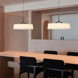 "Two pendant lights with wide fabric shades hang above a modern dining table with black chairs."