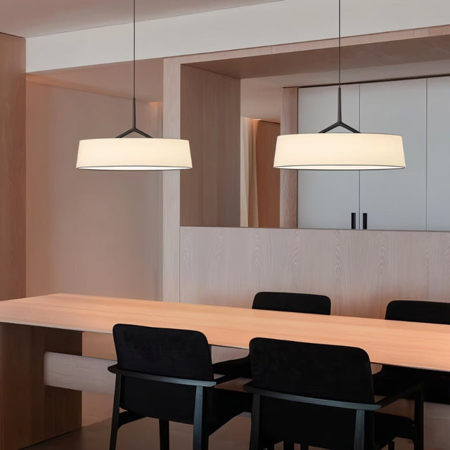 "Two pendant lights with wide fabric shades hang above a modern dining table with black chairs."
