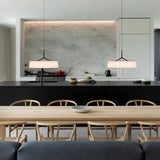 "Two pendant lights with wide, white fabric shades hang over a kitchen island with a black countertop."