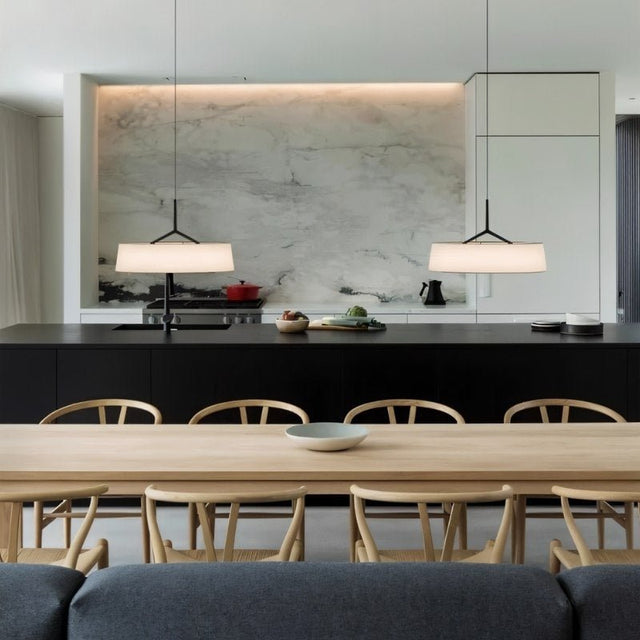 "Two pendant lights with wide, white fabric shades hang over a kitchen island with a black countertop."