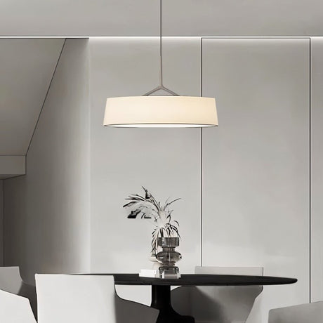 "A minimalist pendant light with a wide, white fabric shade hangs above a round dining table in a modern, neutral-toned room."