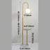 Gold arc floor lamp with white globe light and integrated marble side table on white background.
