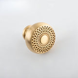 "A gold brass geometric knob with a lattice and sunburst design, shown at an angle on a light background."
