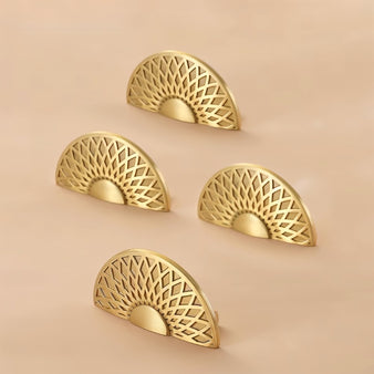 "Four gold brass geometric knobs with a lattice and sunburst design arranged on a beige background."