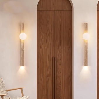 "Pair of minimalist rectangular travertine wall lamps with frosted globe lights, mounted on a hallway wall flanking a wooden double door, providing soft ambient lighting."