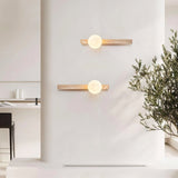 "Pair of minimalist rectangular travertine wall lamps with frosted globe lights, mounted on a white living room wall, providing soft ambient lighting, with a chair and plant in the foreground."