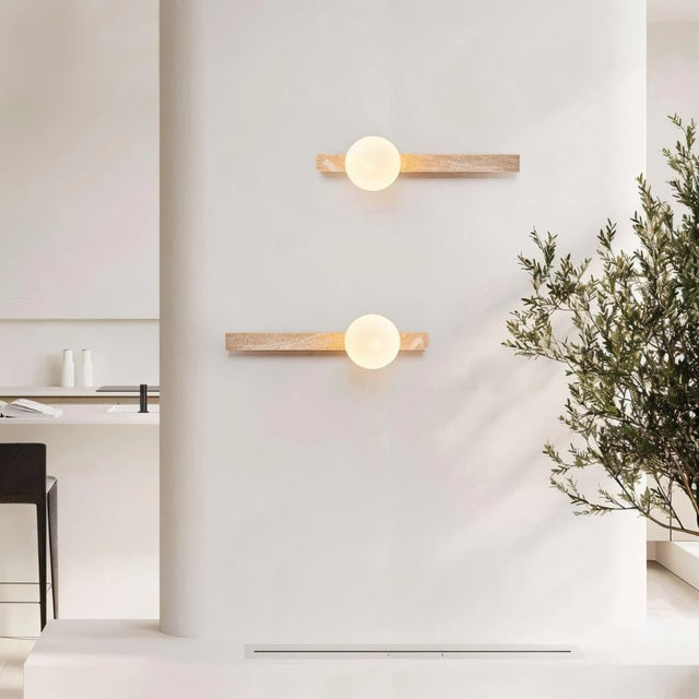 "Pair of minimalist rectangular travertine wall lamps with frosted globe lights, mounted on a white living room wall, providing soft ambient lighting, with a chair and plant in the foreground."