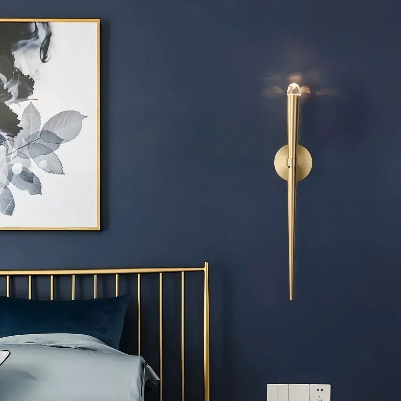 "Modern gold wall lamp with a tapered design and crystal accent, providing soft lighting in a contemporary bedroom."