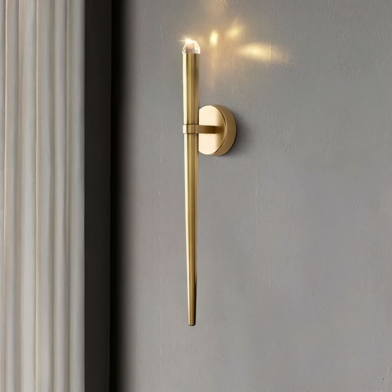 "Modern wall lamp with a tapered gold body and crystal top, providing accent lighting in a contemporary living room."