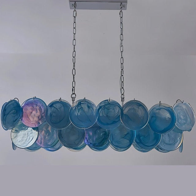 "A modern, rectangular chandelier with cascading blue and iridescent glass discs, illuminated and suspended by chains."