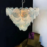 "A modern, round chandelier with cascading blue and iridescent glass discs, hanging in a living room with a chair."