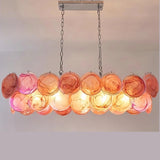 "A modern, rectangular chandelier with cascading orange and pink iridescent glass discs, illuminated and suspended by chains."