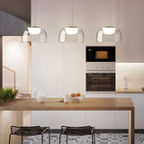 "Three modern pendant lights with clear glass dome shades, hanging above a kitchen island with a wooden countertop and bar stools."