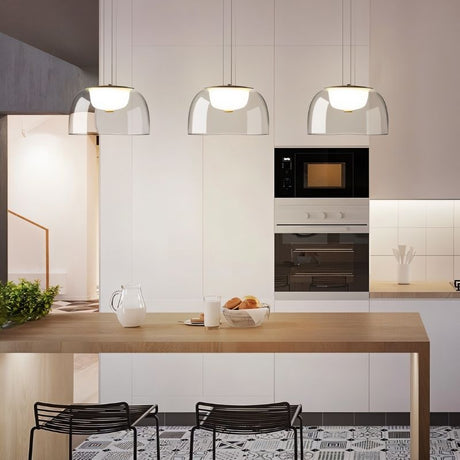 "Three modern pendant lights with clear glass dome shades, hanging above a kitchen island with a wooden countertop and bar stools."
