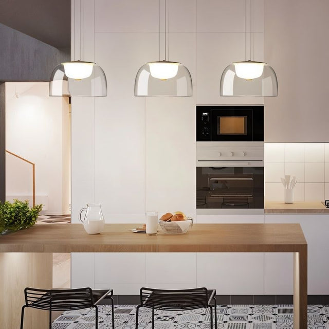 "Three modern pendant lights with clear glass dome shades, hanging above a kitchen island with a wooden countertop and bar stools."