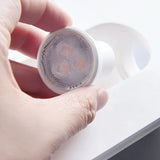 "Hand holding a small LED bulb near a white gypsum Onexa trimless wall light with a circular cutout."