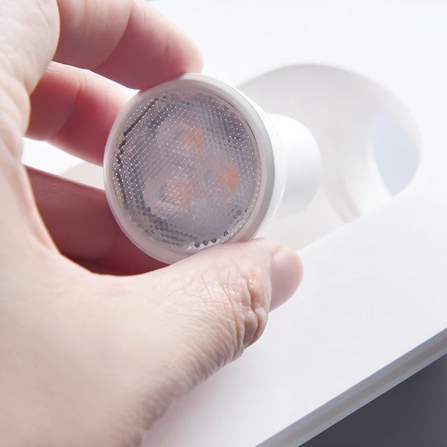 "Hand holding a small LED bulb near a white gypsum Onexa trimless wall light with a circular cutout."