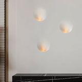 "Three white gypsum Onexa trimless wall lights with dome-like profiles, casting ambient light on a wall above a modern cabinet."