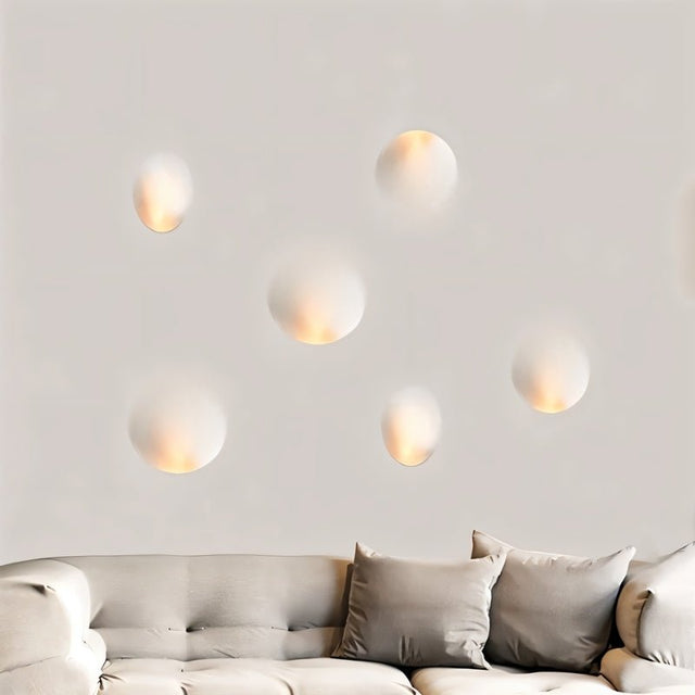 "Multiple white gypsum Onexa trimless wall lights with dome-like profiles, casting ambient light on a wall above a sofa."