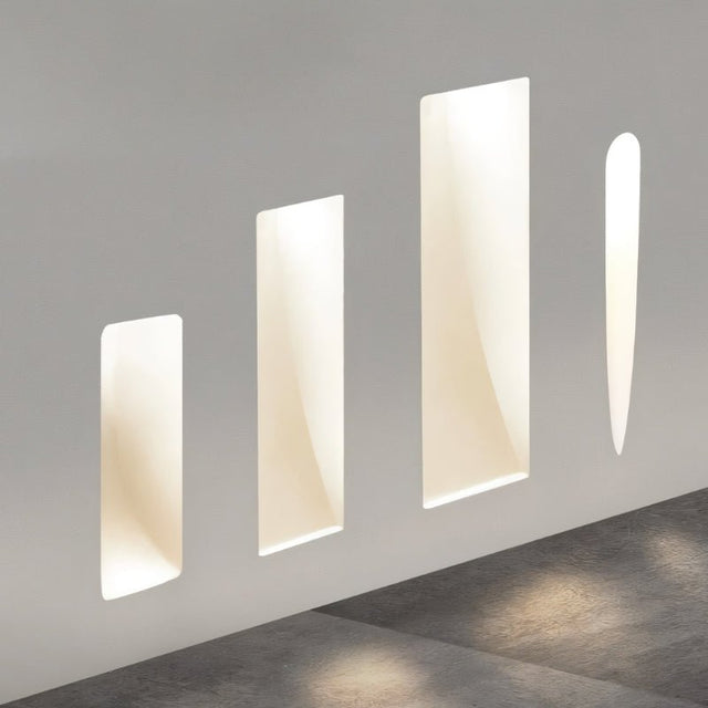 "Four white gypsum Onexa trimless wall lights with varying rectangular and slit cutouts, casting ambient light on a wall."