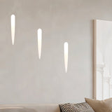 "Three white gypsum Onexa trimless wall lights with elongated slit cutouts, casting ambient light on a wall above a sofa."