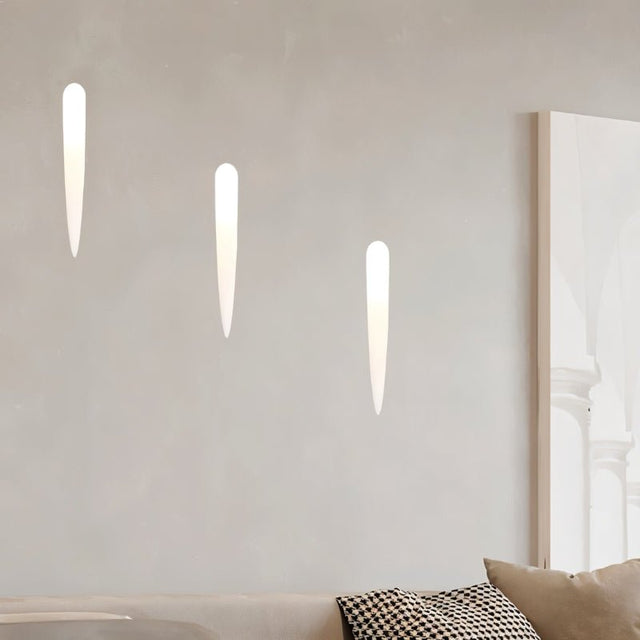 "Three white gypsum Onexa trimless wall lights with elongated slit cutouts, casting ambient light on a wall above a sofa."