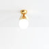 Brass ceiling light fixture with frosted white globe and curved brass arms against a white background.