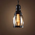 Black metal pendant light with clear glass shade and glowing Edison-style filament bulb against warm brown background.
