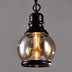 Black metal pendant light with amber glass globe shade and vintage Edison-style bulb, suspended against gray background.