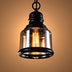Black metal pendant light with clear glass shade and glowing Edison-style bulb against warm tan background.