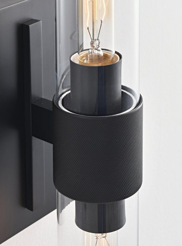 "Close-up detail of a modern black wall lamp with a cylindrical glass shade, showcasing its intricate design and texture."