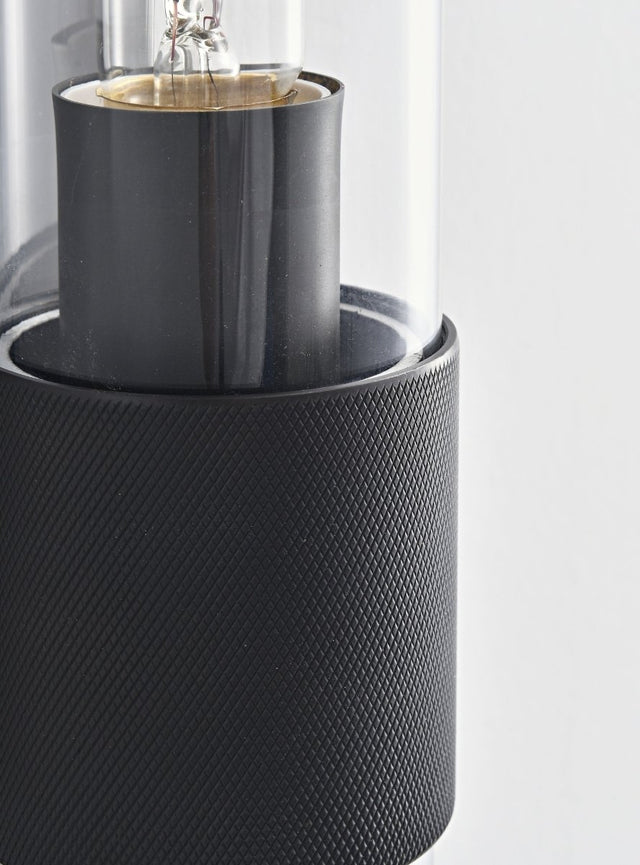 "Close-up detail of a modern black wall lamp with a cylindrical glass shade, showcasing its intricate design and texture."