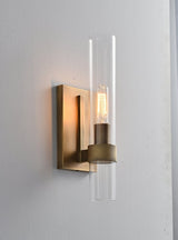 "A modern brass wall lamp with a cylindrical glass shade, blending vintage and contemporary styles with a bronze finish and black accents."