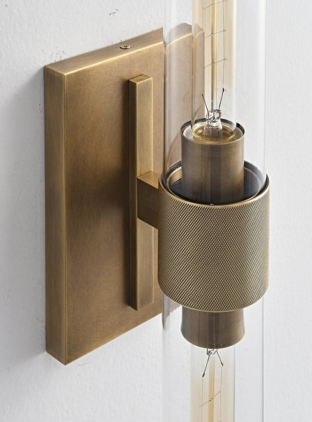 "Close-up detail of a modern brass wall lamp with a cylindrical glass shade, showcasing its intricate design and texture."