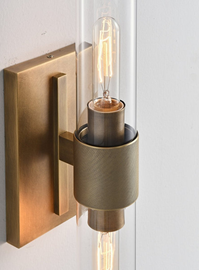 "Close-up detail of a modern brass wall lamp with a cylindrical glass shade, showcasing its intricate design and texture."