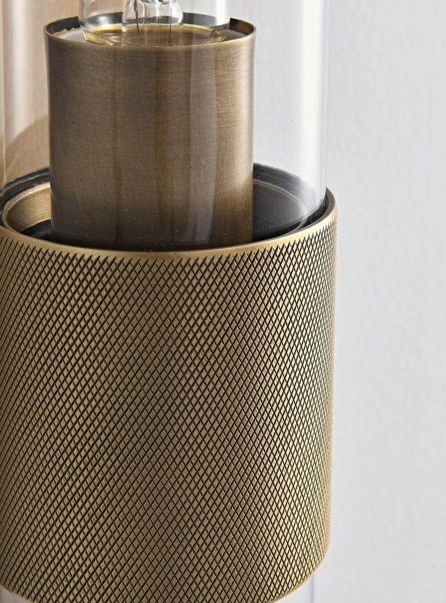 "Close-up detail of a modern brass wall lamp with a cylindrical glass shade, showcasing its intricate design and texture."