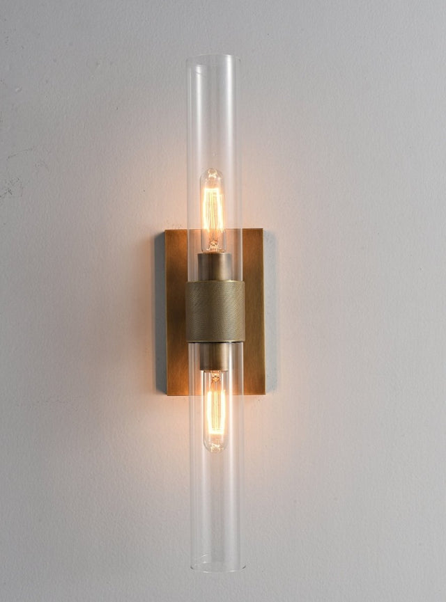 "A modern brass wall lamp with a long, vertical cylindrical glass shade, showcasing a bronze finish with black accents, blending vintage and contemporary styles."